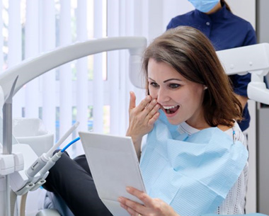 Dental patient holding mirror, admiring the results of her treatment
